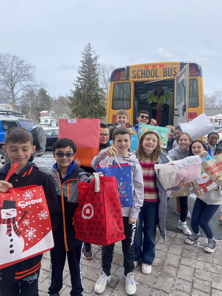 .Female and Male 4th grade students with presents on hand  while posing in front of the school bus that will take them to drop off their giving tree donations 