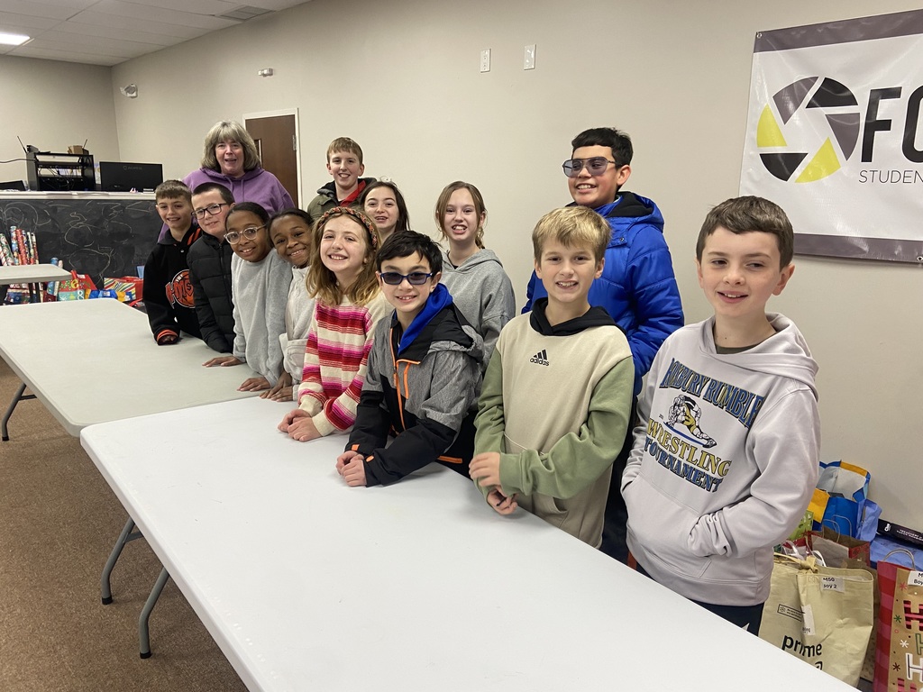 Female and Male 4th grade students with an adult female . All 12 students  and Female adult volunteer posing at a table all smiles 