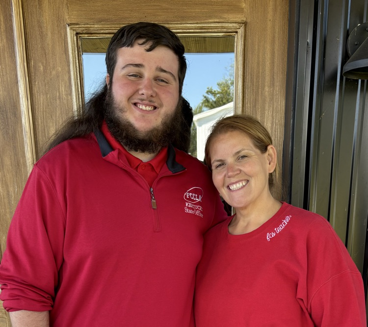 A teenage male student stands next to his female teacher