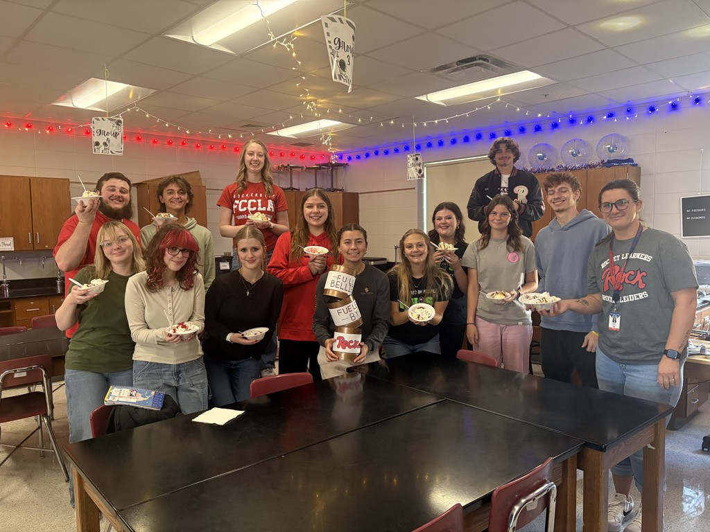 A crowd of high school students stand in a science classroom holding bowls of ice cream.