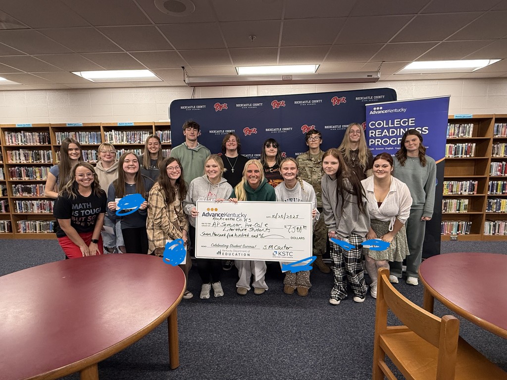 A group of high school students stand in front of a blue background holding a large cardboard check.  