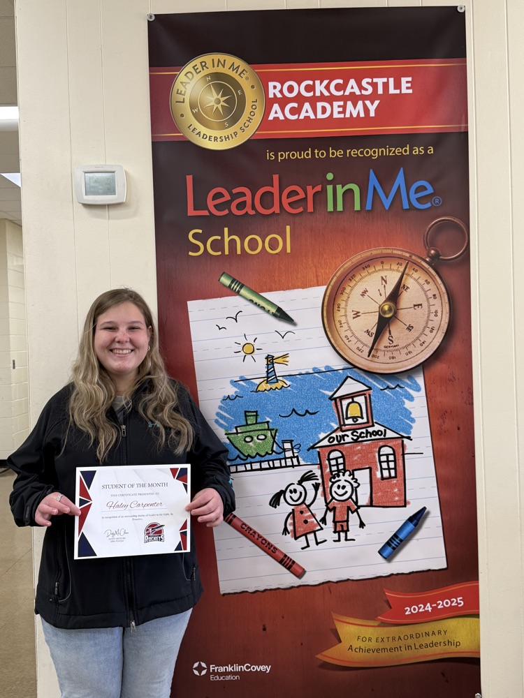 A female high school students holds a certificate and stands beside a Leader in Me poster.