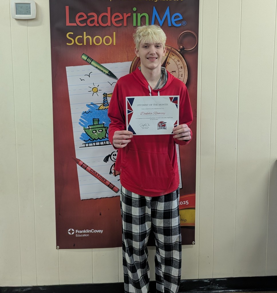 A young man in a red shirt and plaid pants stands holding a certificate. 