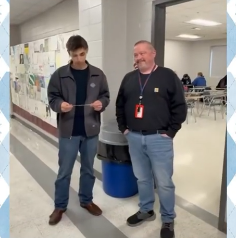 A high school aged male looks down at a slip of paper in his hands. 