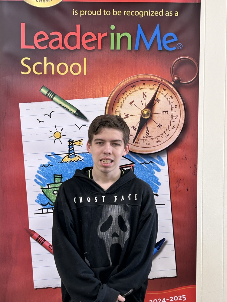 A young man stands smiling in front of a banner.  