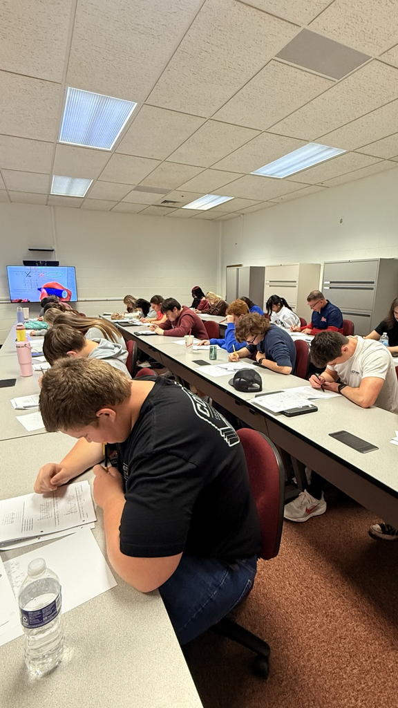 Students lean over a table writing.  