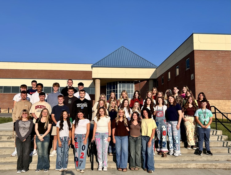 Students stand in a group on steps leading to a brick building.