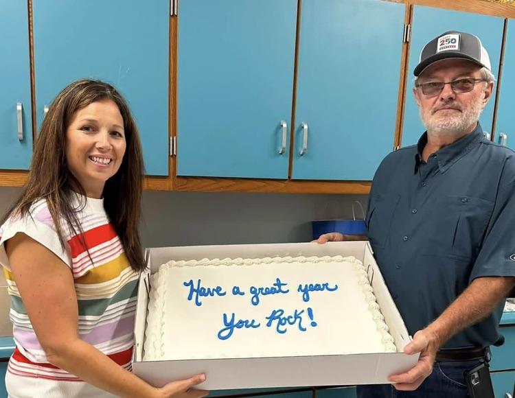 Two people hold a large cake between them.