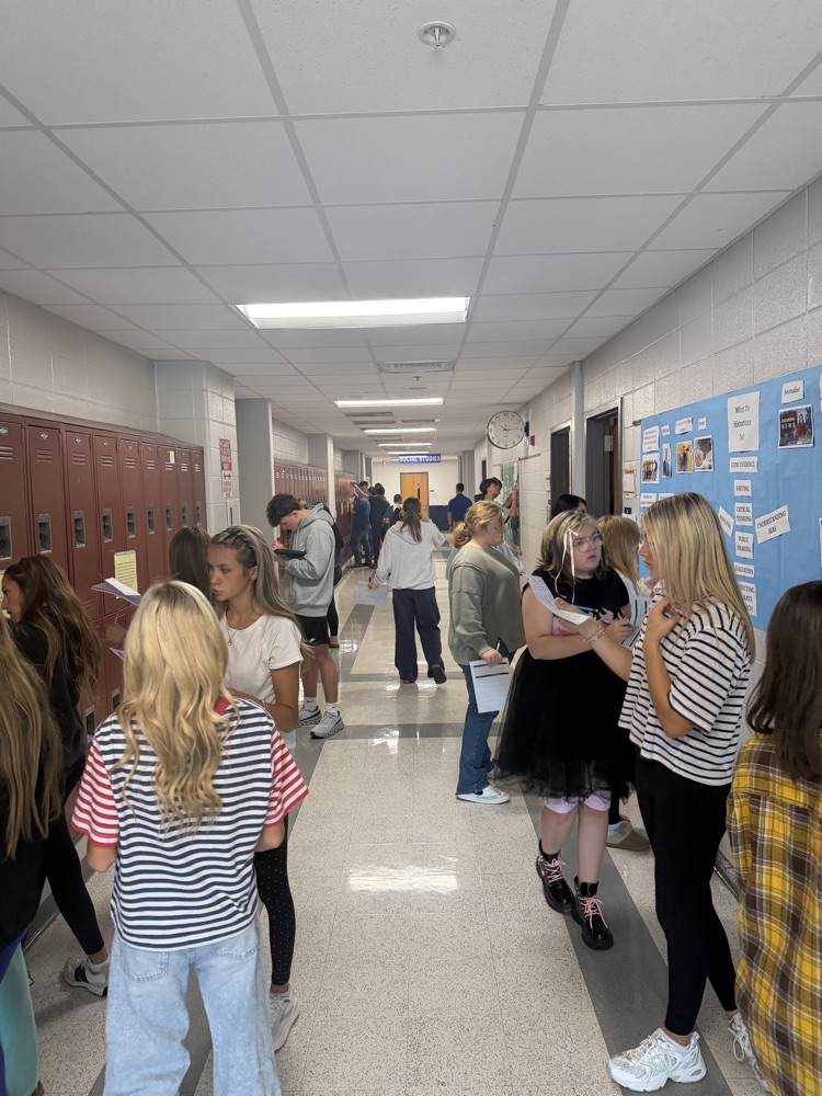A long shot of a student-filled hallway. Students look at images hung on the walls.