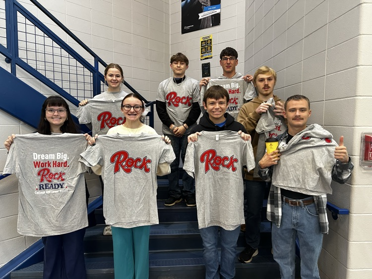 Students stand on steps holding t-shirts.  