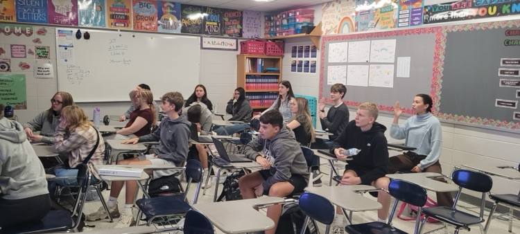 Students sit in desks.  The desks are in rows  