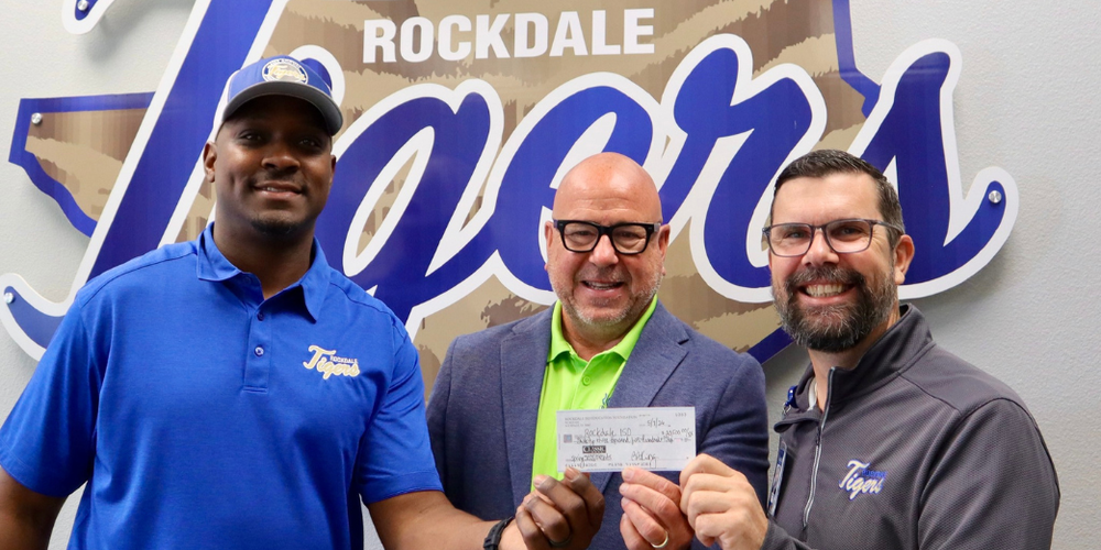 three men holding a check in front of the Rockdale Tigers logo