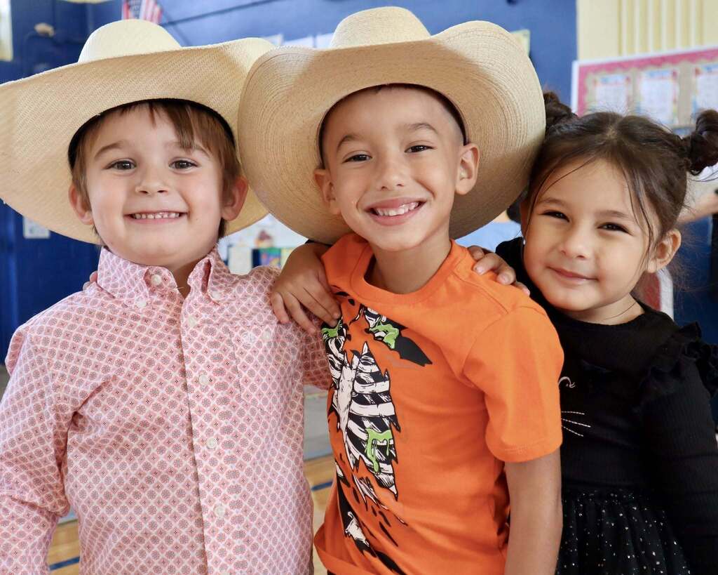 Three children in cowboy hats standing together, smiling