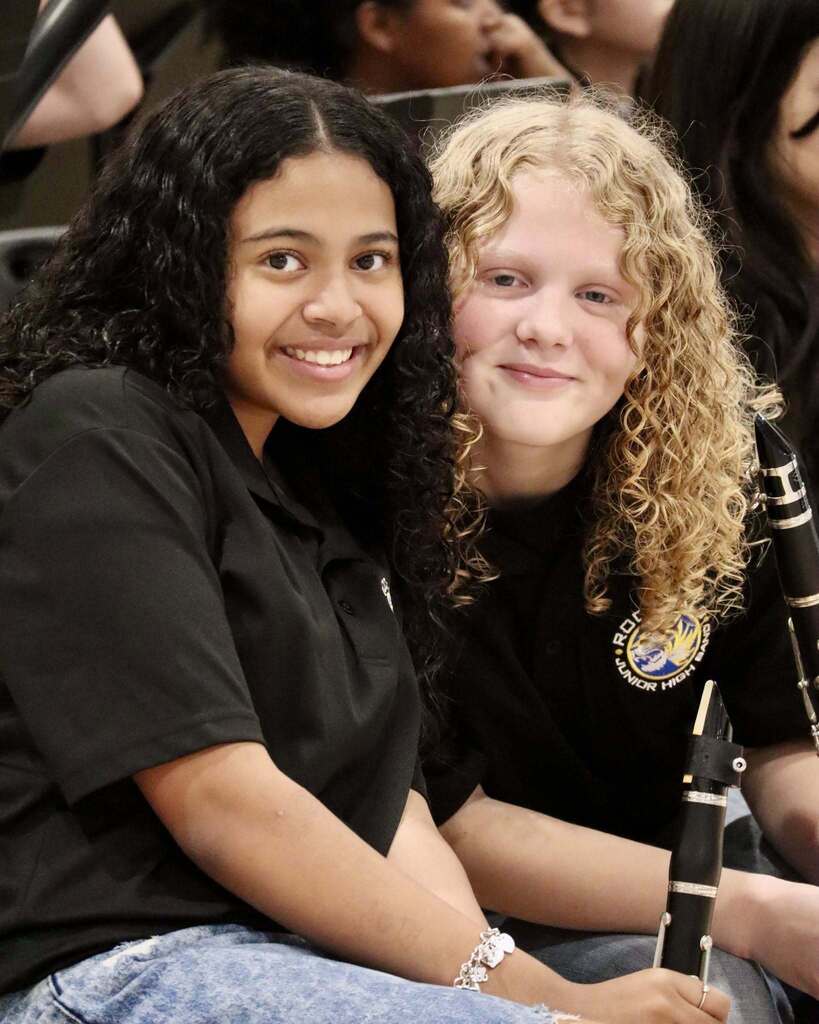 Two students dressed in black sitting together and smiling.