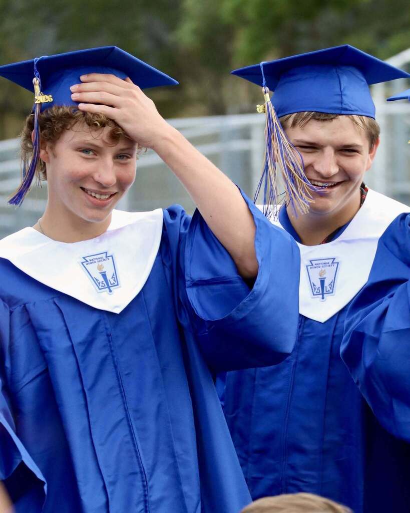 Two students in graduation gowns standing together and smiling