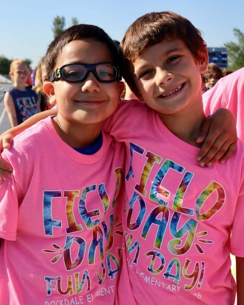 Two students in pink field day shirts standing together and smiling.