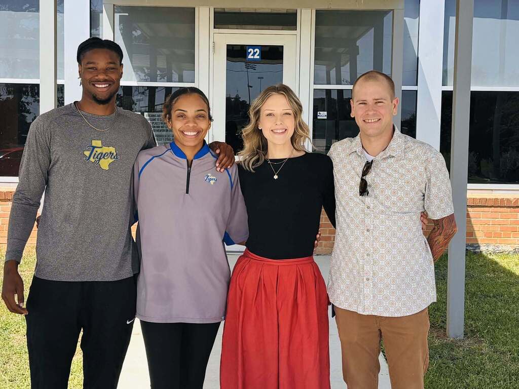 Four people standing outside together and smiling.