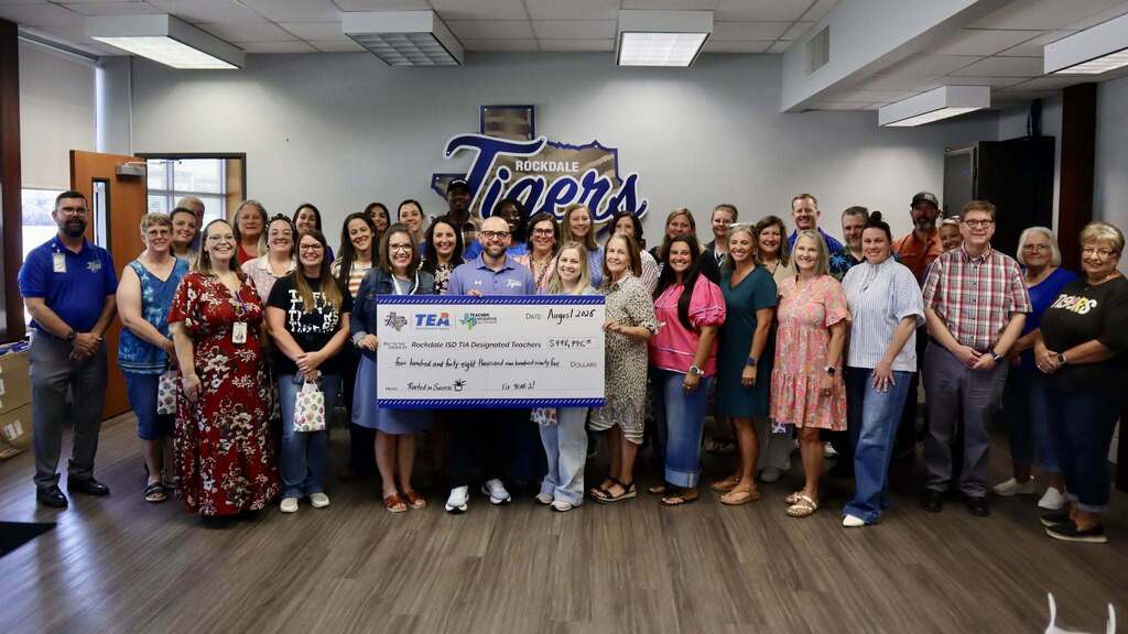 A group of teachers standing together, holding a large check and smiling.