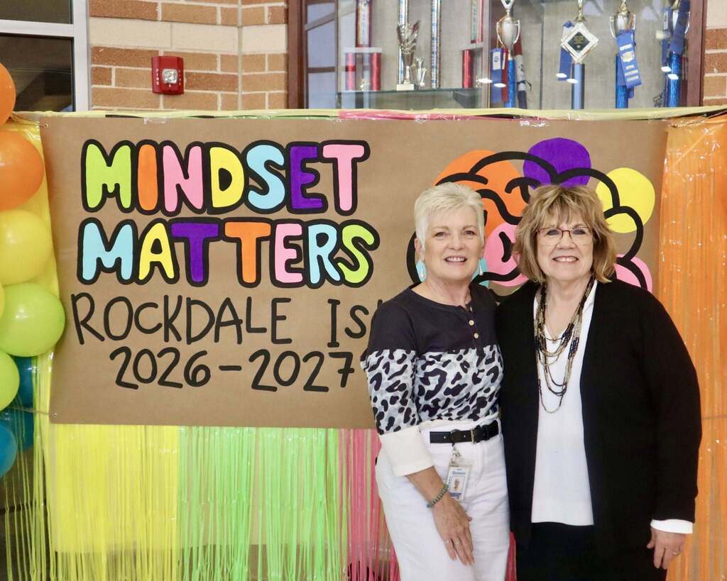 Two women standing together and smiling in front of a sign that says "Mindset Matters"