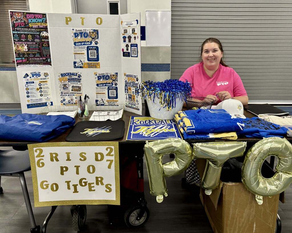 Woman behind PTO exhibit table sitting and smiling.