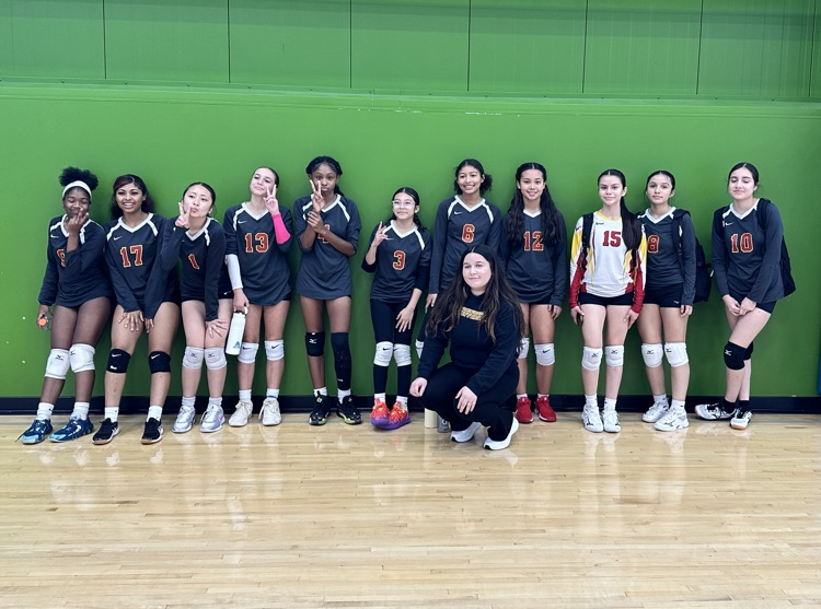 Jefferson freshman volleyball team poses in front of a green gym wall after the Guilford Tournament, smiling in black and red uniforms.