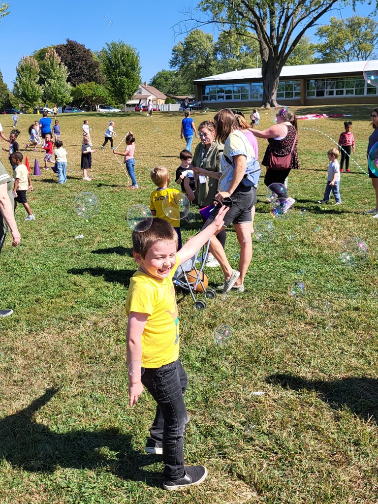Boy playing with bubbles in a field with other students playing.