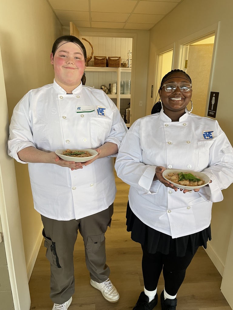 Two students holding up their bowls of pasta 