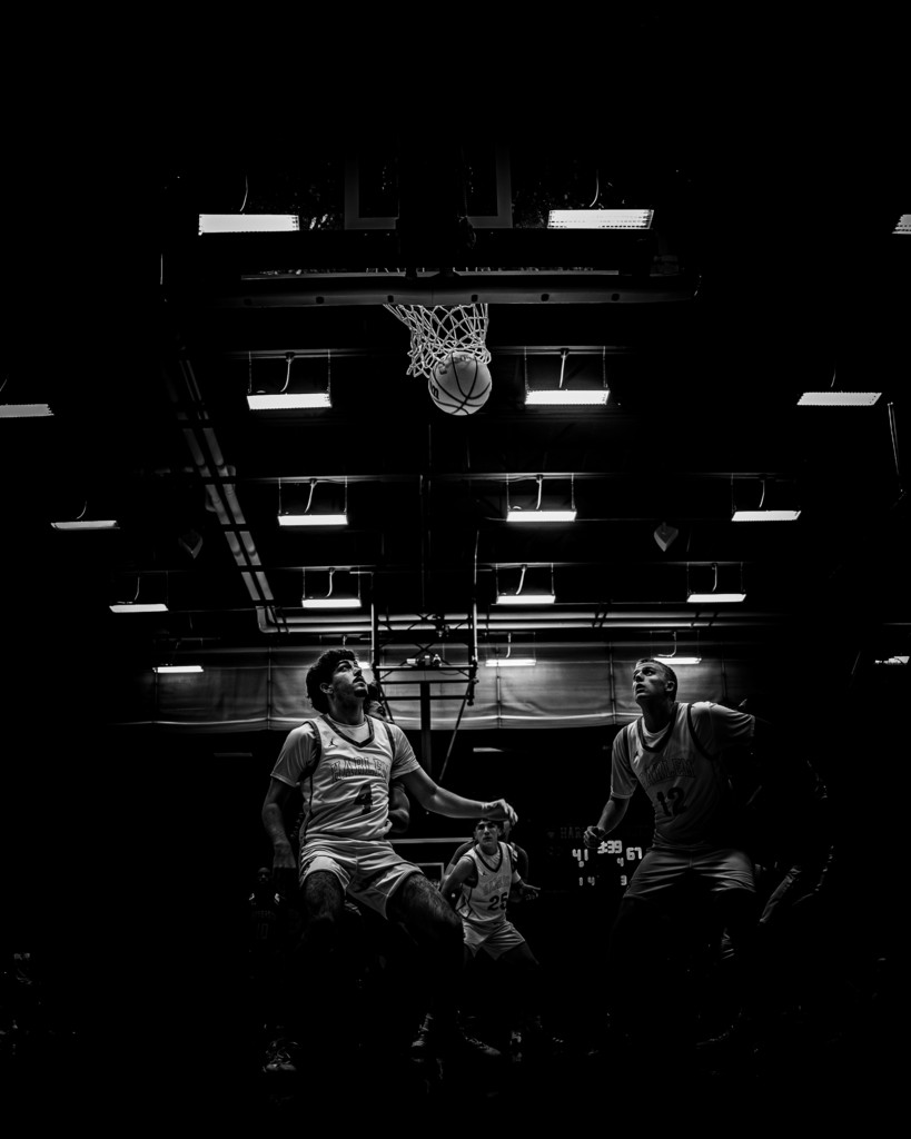 Two students are standing underneath the basketball rim waiting for the ball to drop. As it falls through the net.