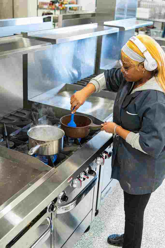 A student is stirring their food in a pot that is on the stove.