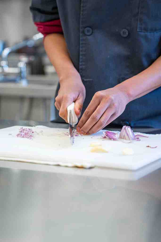 A detail shot of a knife cutting into an onion.