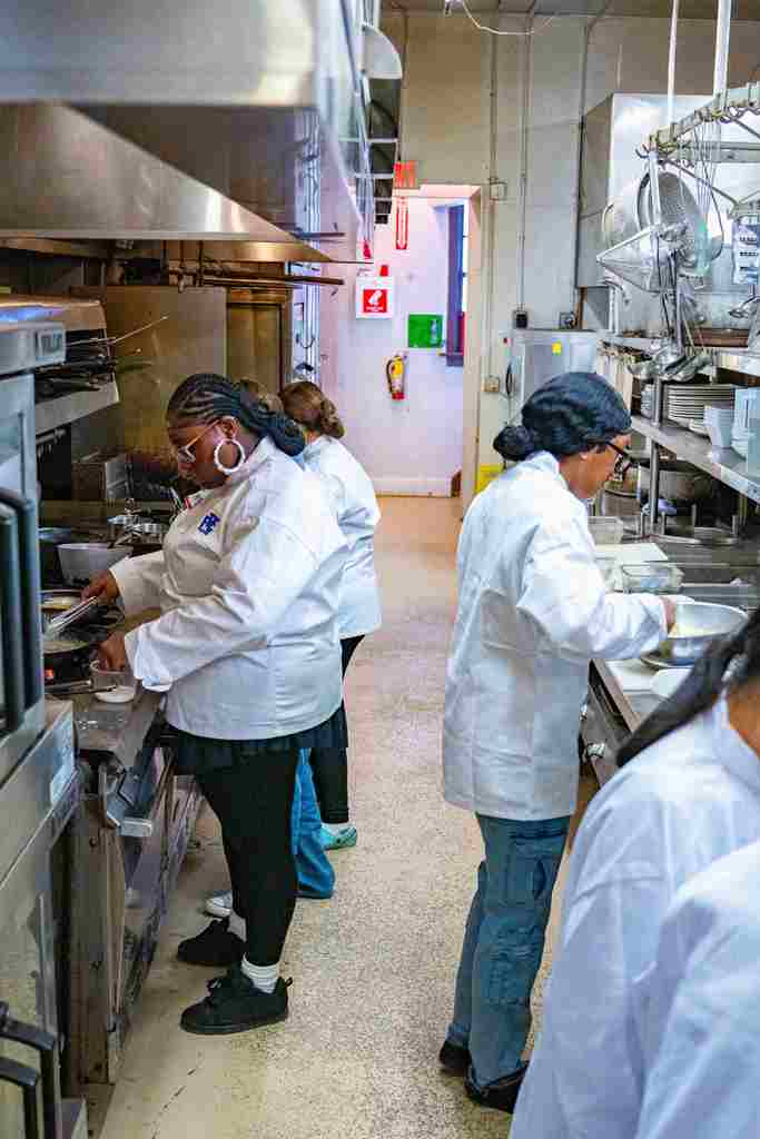 Various students cooking at the stoves and preparing food.