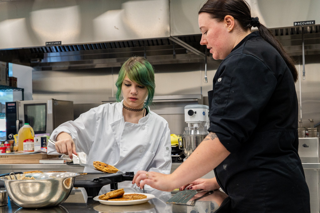Student is cooking pancakes and is assisted by the teacher.