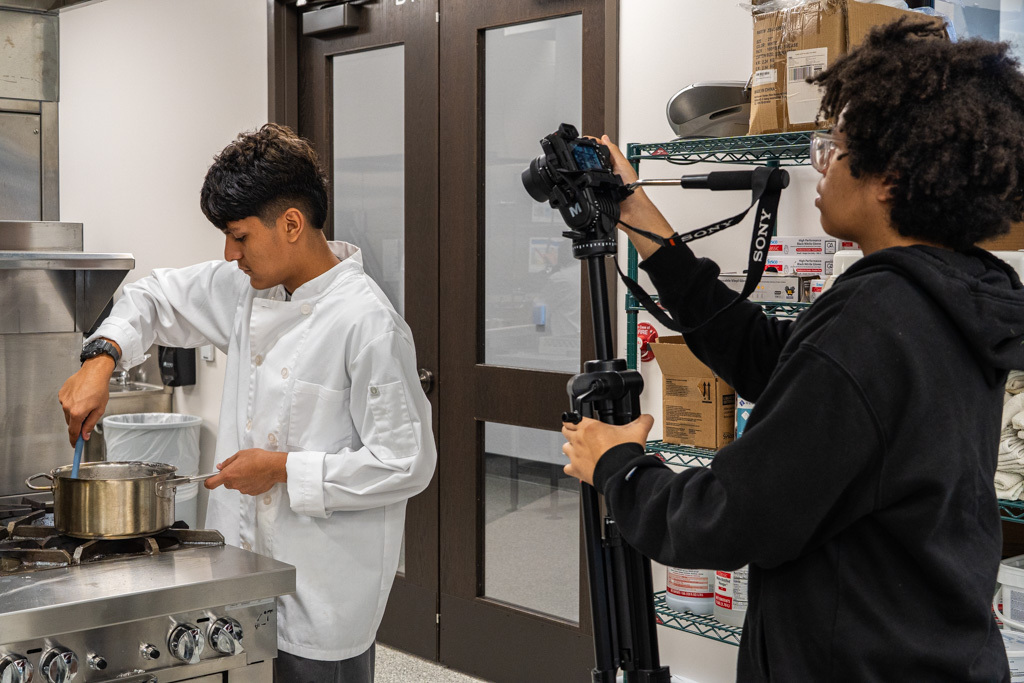 Student is cooking and another student is filming them.