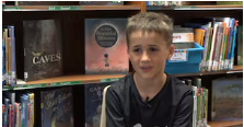 Boy in black shirt sitting in library in front of book shelves with books on the shelves