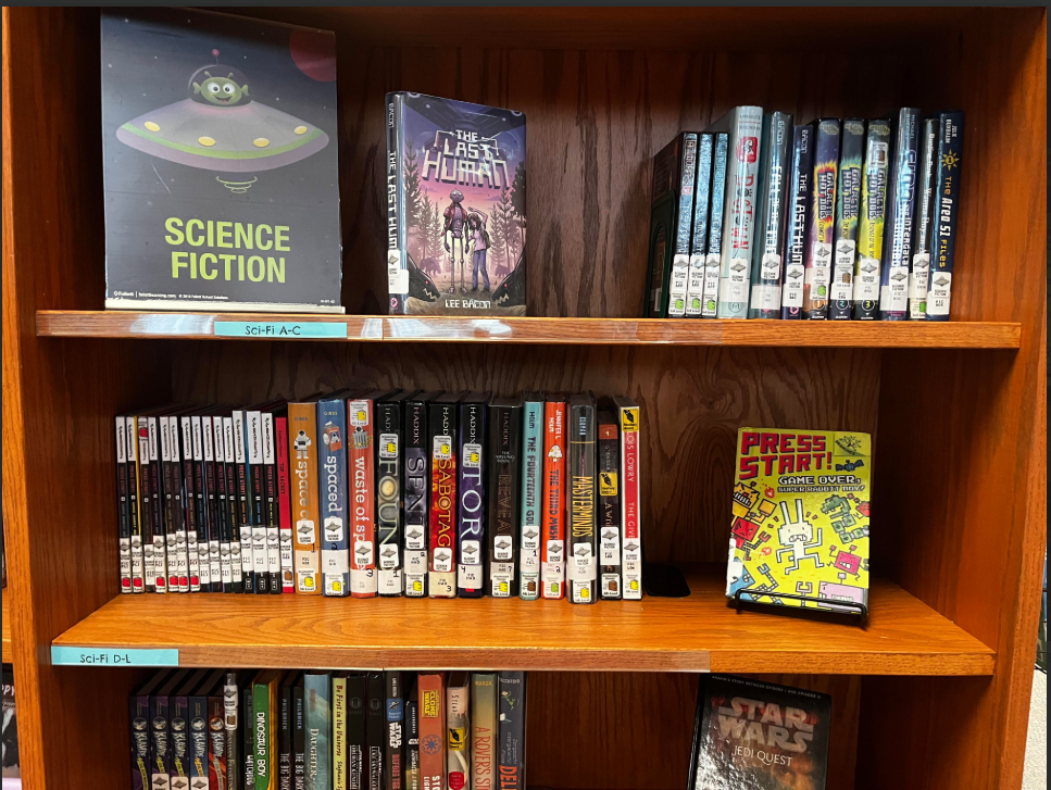 Books on a library shelf with a Science Fiction sign that has an alien spaceship