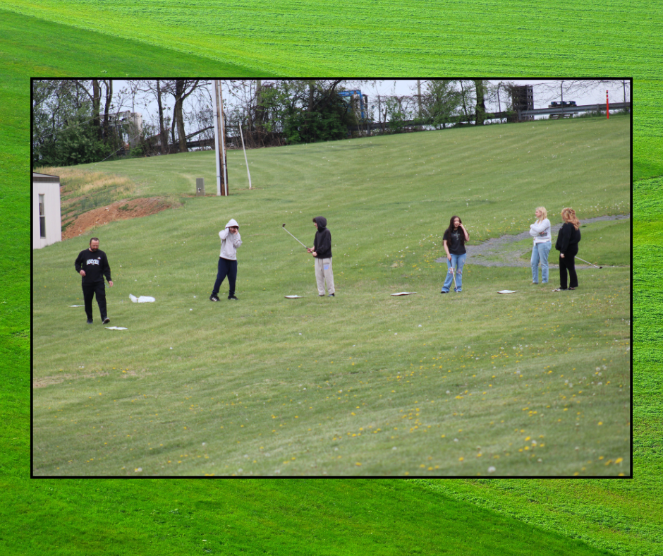 A group of people on a golf course, some with golf clubs, on a sunny day.