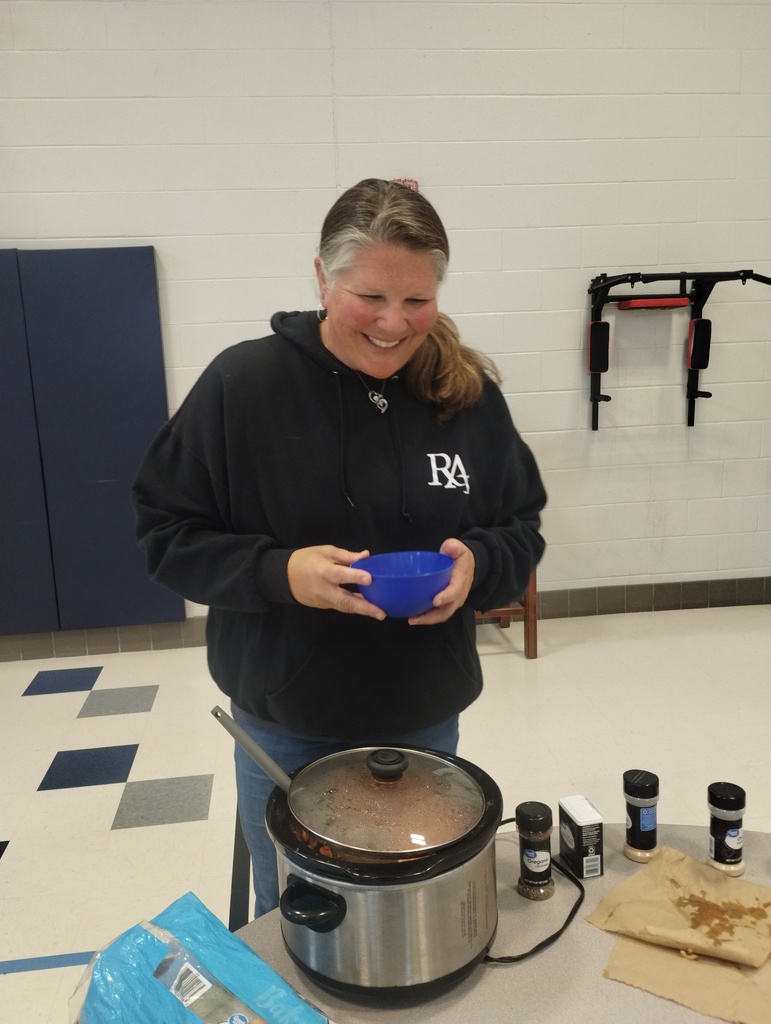 A woman wearing a black hoodie holds a blue bowl in front of a crockpot on a table.