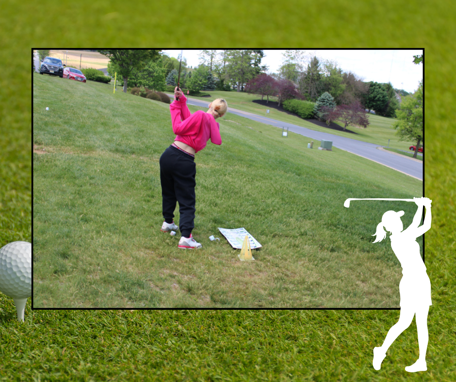 Person dressed in pink shirt and black pants practices golf on a lawn with green grass.