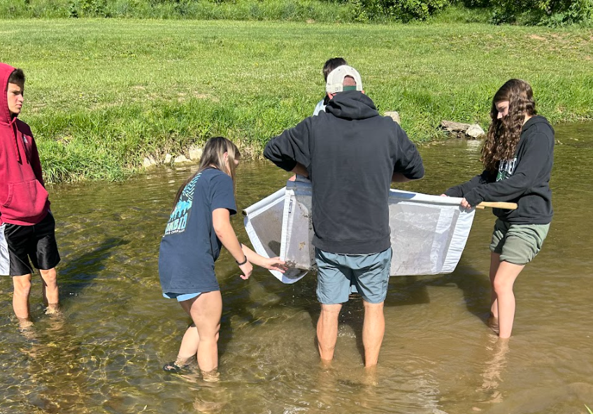 Five individuals standing in a river holding a net, likely conducting a water study.