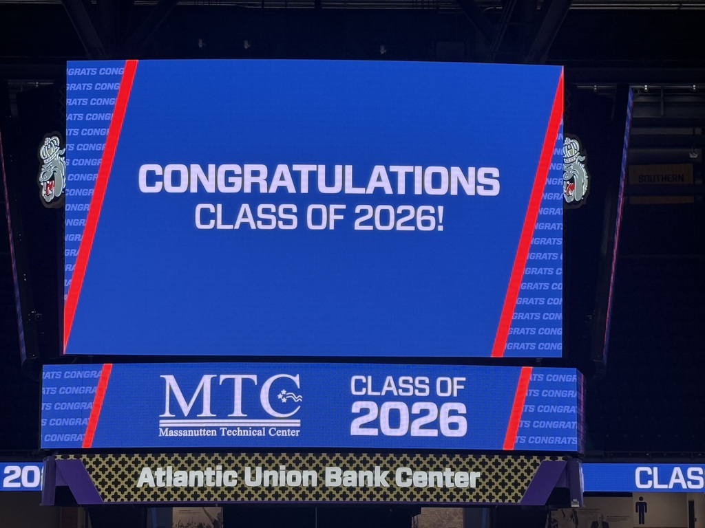 A large blue electronic display reads "Congratulations Class of 2026" with smaller text below it. It is located in a sports venue.