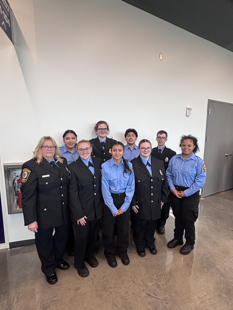 A group of uniformed individuals, possibly police or firefighters, stand together in a room with white walls.
