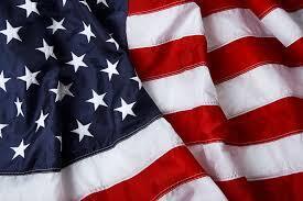 American flag with blue field, stars, and 13 red and white stripes. Background of flag is blurred.