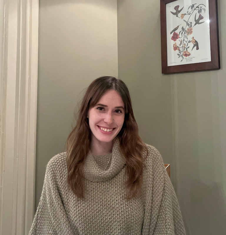 Ms. MacDonald is pictures wearing a tan sweater in her home. 