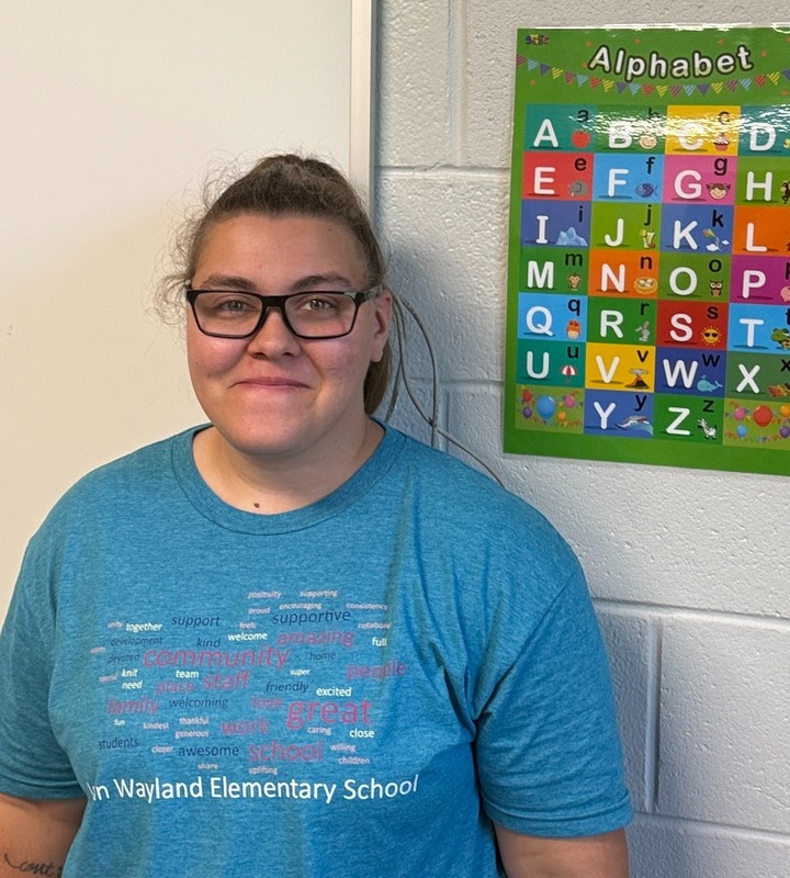 Ms. Foster is pictured wearing a blue JWES shirt info front of white wall. 