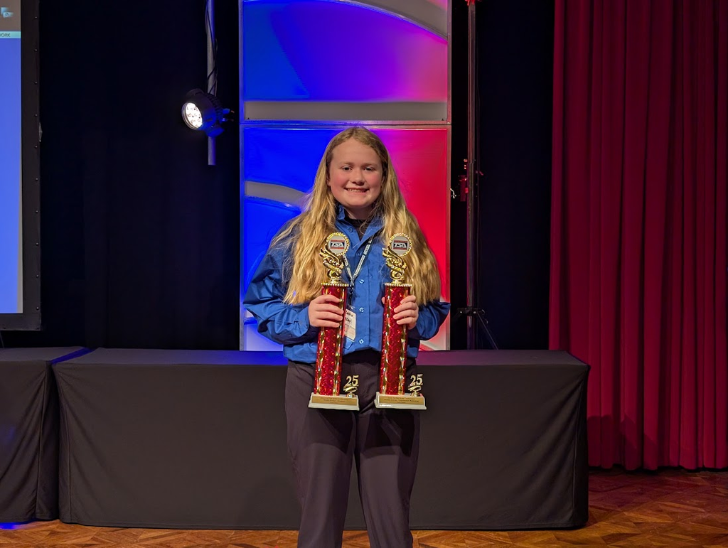 student on stage holding trophies