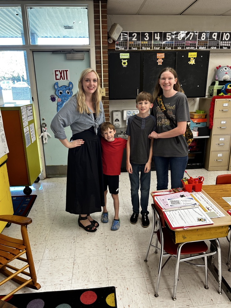 teacher smiles with two students and their mom