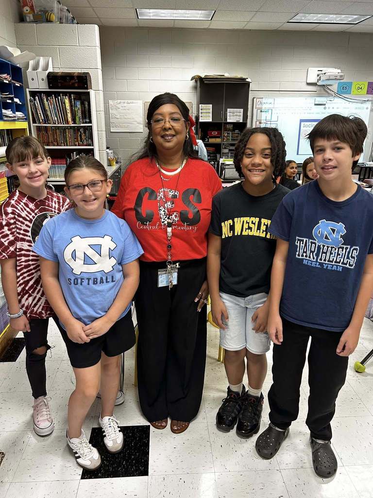 Four students stand with teacher sporting their favorite team logos on their shirts