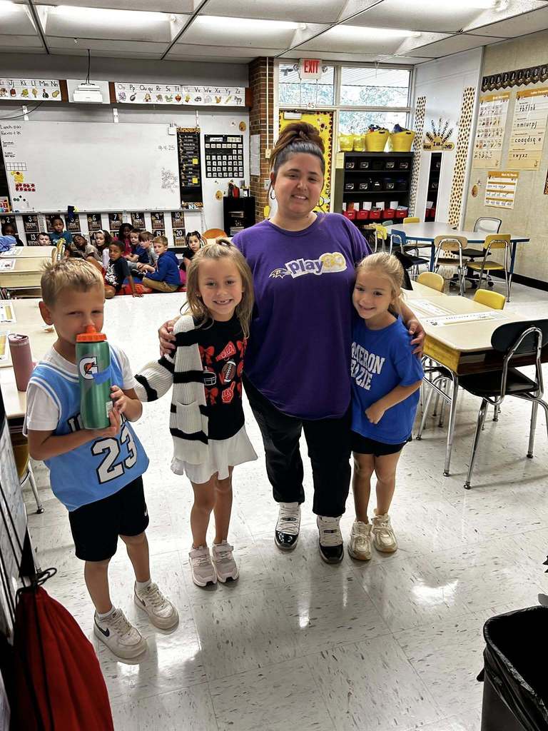 Three students stand with teacher sporting their favorite team logos on their shirts