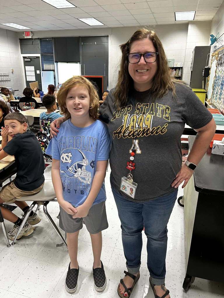 A student stands with a teacher sporting their favorite team logos on their shirts