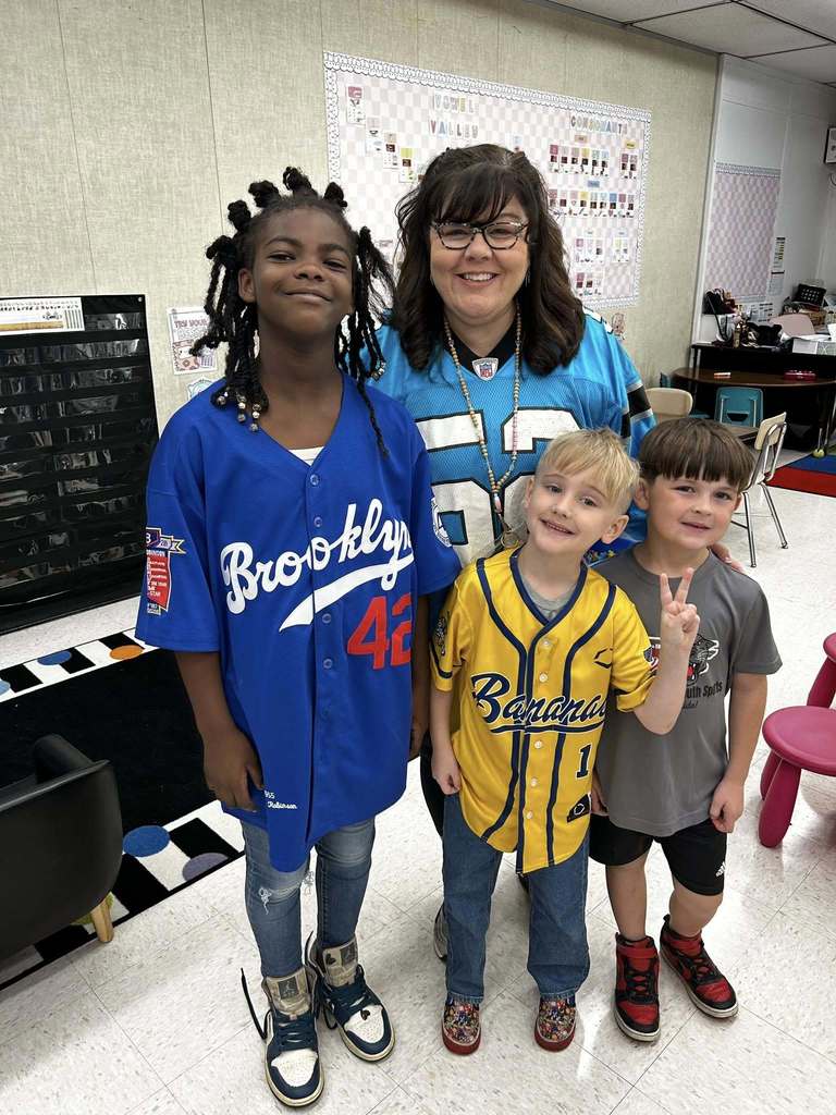 Teacher stands with three of her students sporting their team shirts. 